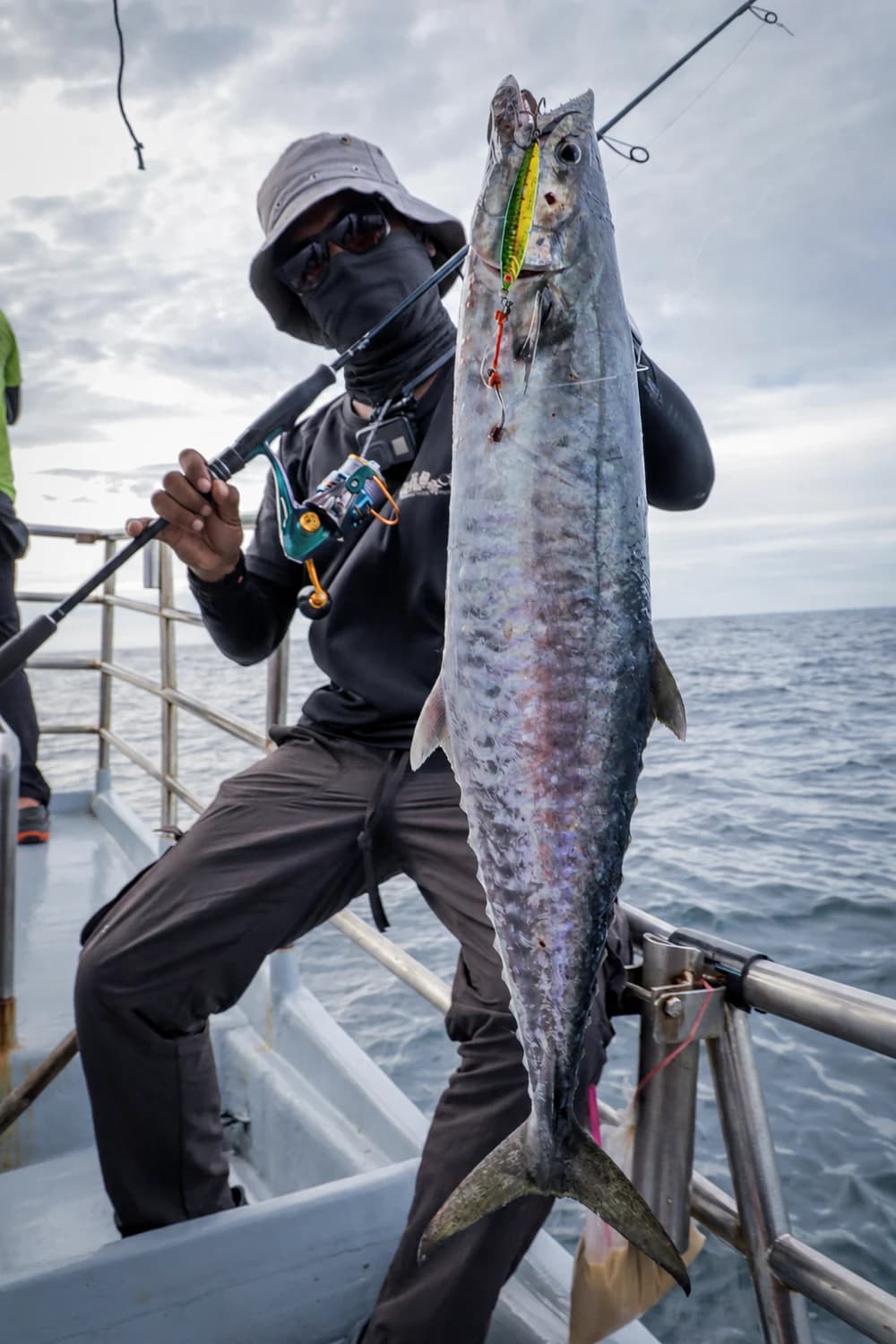 An offshore angler holding a long silver fish, with rod and reel in hand.
