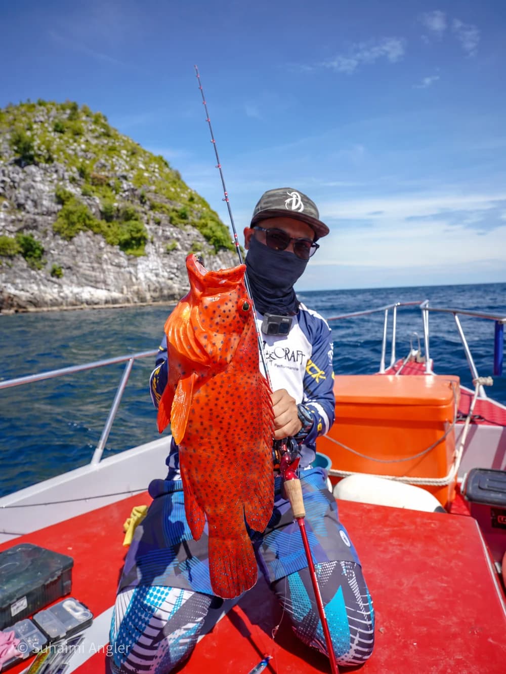 An angler holding an orange-spotted fish aboard a boat.