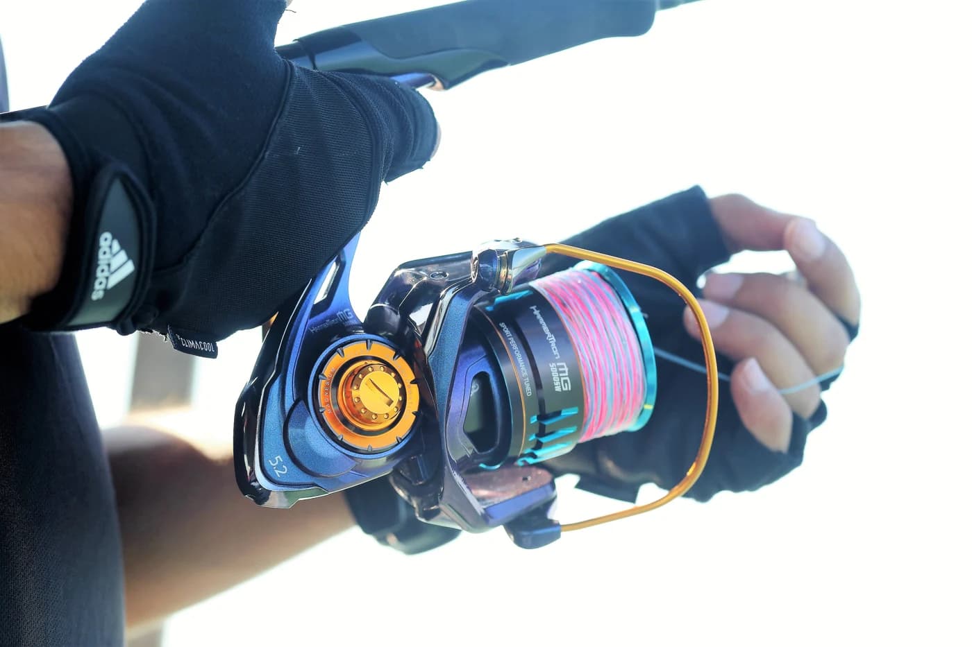 Gloved hands operating a blue and gold reel on the water.