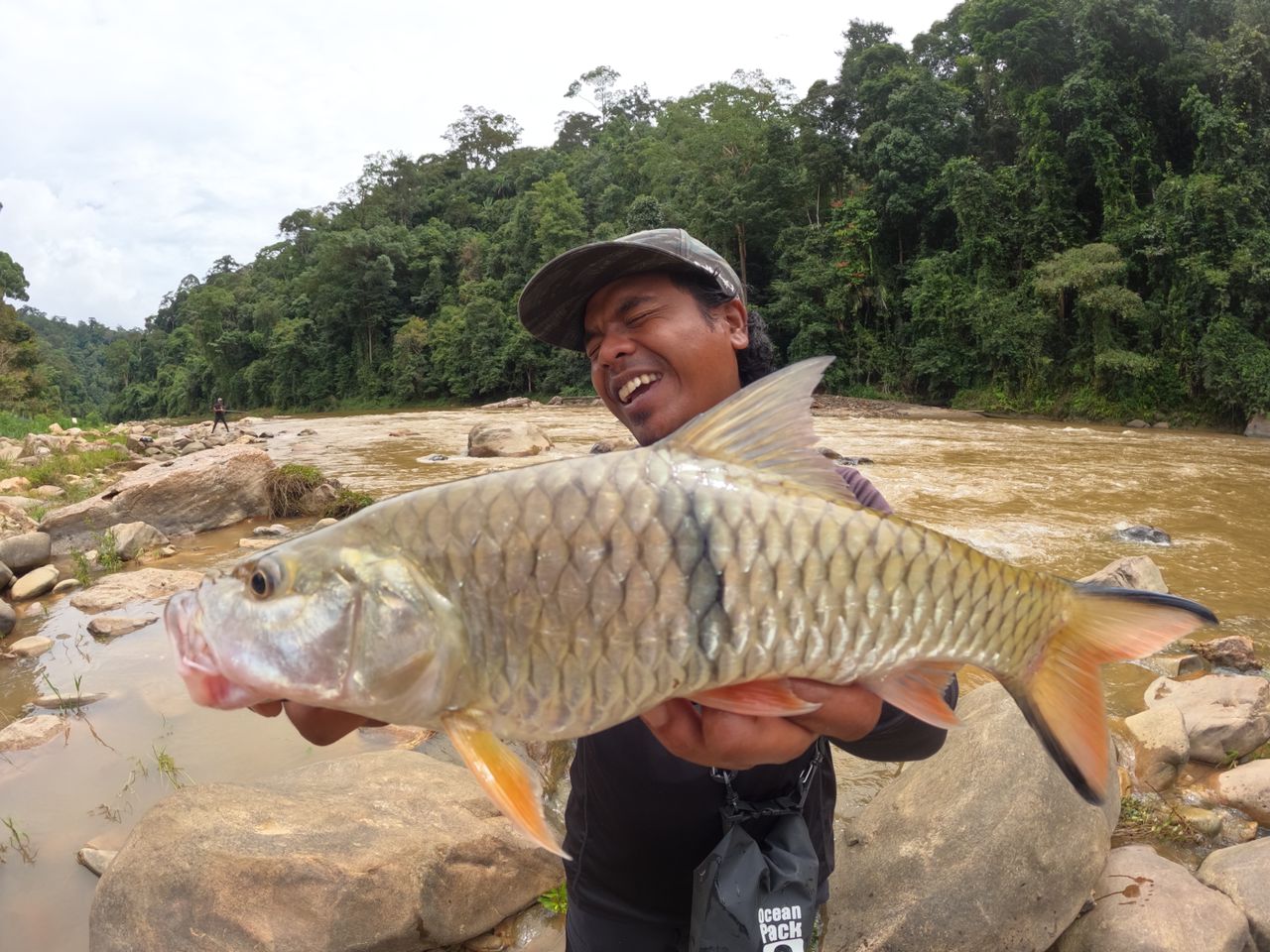 An angler with a sebarau at a rocky riverbank